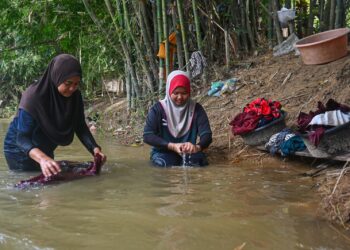 PENDUDUK membasuh pakaian yang diselaputi lumpur akibat banjir di Kampung Pasir Raja, Hulu Dungun, Dungun, hari ini. - UTUSAN/PUQTRA HAIRRY ROSLI