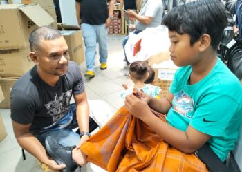 MUHAMMAD Aiman Hariz Mahabizan dibantu ayahnya, Mahabizan Razal memakai kasut sekolah baharu pada program Kembali Ke Sekolah anjuran Fisabilillah di  Kuala Terengganu, hari ini. - UTUSAN/KAMALIZA KAMARUDDIN
