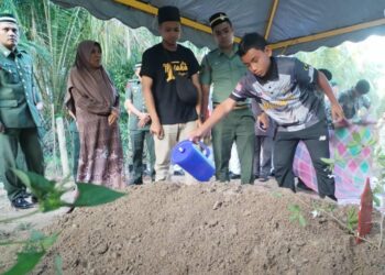 MUHAMMAD Nabil menyiram air mawar di pusara ayahnya, Rozali Abdull Rani di Tanah Perkuburan Islam Gong Bayor, Besut, pagi ini. - UTUSAN/WAN ZURATIKAH IFFAH WAN ZULKIFLI