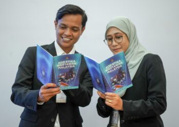 PEGAWAI Penerangan Media, Muhammad Syamil Zulkhairi dan Aisyah Lokman melihat buku Kod Etika Wartawan Malaysia pada Majlis Peluncuran Kod Etika Wartawan Malaysia di Kementerian Komunikasi, Putrajaya. - UTUSAN/FAISOL MUSTAFA