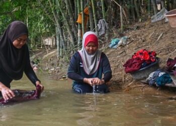 PENDUDUK membersihkan pakaian yang diselaputi lumpur akibat banjir di Kampung Pasir Raja, Hulu Dungun, Dungun, semalam. – UTUSAN/PUQTRA HAIRRY ROSLI