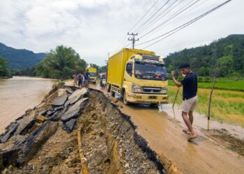SEORANG lelaki membantu lori melalui kawasan jalan yang rosak akibat banjir kilat di daerah Pesisir Selatan, Sumatera Barat.-AFP