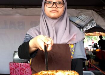 KHATIJAH Isa menunjukkan asam  pedas ikan jenahak yang dijual di Bazar Ramadan Bandar Kampar baru-baru ini. - UTUSAN