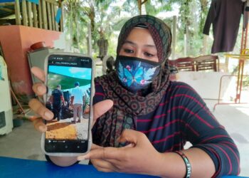 NORAINI Alwi menunjukkan gambar suasana ketika upacara pengebumian Muhamad Sufian di Pulau Bintan, Indonesia, baru-baru ini.