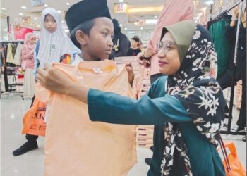 KHADIJAH Mohd. Sani mencuba baju Melayu pada Muhammad Aqil Halif ketika Program Tautan Kasih Ramadan anjuran  Zakat Melaka dan PNMB di Bukit Piatu, Melaka. – UTUSAN/MUHAMMAD SHAHIZAM TAZALI