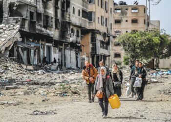 Seorang wanita membawa tong air bersama sebuah keluarga meninggalkan rumah mereka yang musnah 
di Gaza untuk mencari perlindungan di kawasan lain, semalam. – AFP