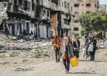 Seorang wanita membawa tong air bersama sebuah keluarga meninggalkan rumah mereka yang musnah 
di Gaza untuk mencari perlindungan di kawasan lain, semalam. – AFP