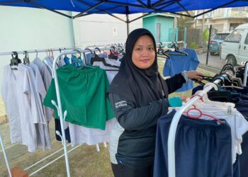 SURIATI Shukor menunjukkan baju sekolah terpakai yang diletakkan di luar Stesen Petronas Papar, Sabah semalam.