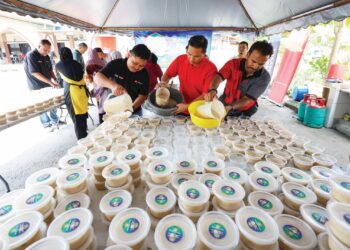 Kakitangan Media Mulia bersama Agrobank menuang bubur lambuk ke dalam bekas pada program Kongsi Berkat Bubur di Surau Jumaat Al-Husna Seri Semarak, Kuala Lumpur, baru-baru ini. – UTUSAN/FARIZ RUSADIO