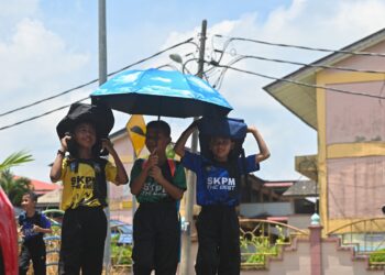 MURID sekolah menutup kepala menggunakan beg dan payung berikutan cuaca panas di pekarangan luar Sekolah Kebangsaan Padang Mengkuang, Marang, baru-baru ini. - UTUSAN/PUQTRA HAIRRY ROSLI