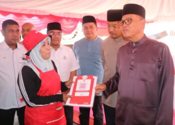 WAN ROSDY Wan Ismail (kanan) menyampaikan paparan kod QR kepada peniaga Bazar Ramadan Sungai Koyan di Dataran Perniagaan Felda Sungai Koyan di Lipis, Pahang. - FOTO/SALEHUDIN MAT RASAD