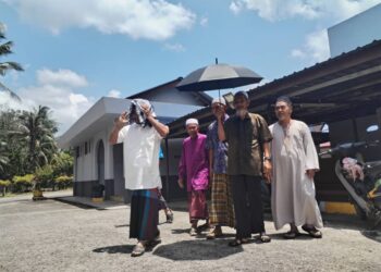 BEBERAPA penduduk menutup kepala menggunakan kain dan berpayung ketika pulang ke rumah selepas selesai menunaikan solat Zohor di Masjid Felda Tenang, di Hulu Besut, Besut, hari ini. - UTUSAN/WAN ZURATIKAH IFFAH WAN ZULKIFLI