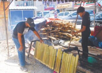 HADRY Helmi (kiri) sedang membetulkan buluh lemang dibantu rakannya di Klebang, Melaka. - UTUSAN/AMRAN MULUP