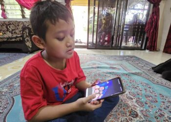 ATTAR Azim melihat gambar kenangannya bersama ibu bapa dan dua adik yang maut dalam nahas di Kuala Krai, Kelantan pada 2 Mac lalu. -UTUSAN/ASLIZA MUSA