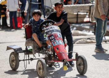 DUA kanak-kanak Palestin menaiki kereta mainan polis buatan sendiri di kem Deir el-Balah di tengah Semenanjung Gaza.-AFP