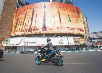 SEORANG lelaki menunggang motosikal melepasi papan iklan yang menggambarkan peluru berpandu balistik Iran di Tehran, semalam. -AFP