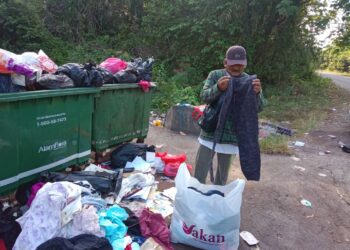 ISMAIL Ahmad menunjukkan sebahagian pakaian terpakai yang dikutip dalam tong sampah' di Jalan Jerantut-Maran berdekatan Kampung Bukit Rang di Jerantut, Pahang. - UTUSAN/HARIS FADILAH AHMAD