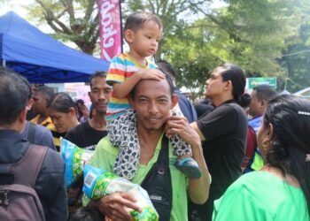 JAMIAN Johari sambil mendukung anaknya tidak melepaskan peluang mendapat beras percuma di tapak niaga Majlis Perbandaran Temerloh, Kuala Krau di Temerloh, Pahang. – UTUSAN/SALEHUDIN MAT RASAD