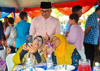 FADZLI Mohamad Kamal (belakang) melayani tetamu yang hadir pada majlis jamuan hari raya Aidilfitri di padang awam Felda Lembah Klau di Raub, Pahang. - UTUSAN/SALEHUDIN MAT RASAD