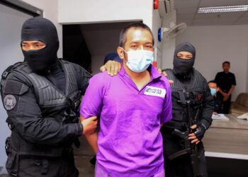 TERTUDUH diiringi oleh anggota polis dari Unit D9 (Bahagian Siasatan Jenayah Berat) lengkap bersenjata semasa tiba di Mahkamah Majistret Kota Bharu, Kelantan hari ini-UTUSAN/KAMARUL BISMI KAMARUZAMAN.