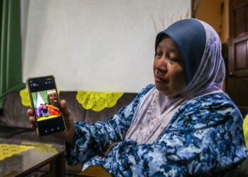 NORYANI Tamadun sebak ketika menunjukkan gambar terakhir bersama arwah adiknya, Muhammad Faisol (baju oren) yang terkorban dalam nahas helikopter di Pangkalan TLDM Lumut ketika ditemui di Kampung Tanjung, Sik. -UTUSAN/SHAHIR NOORDIN