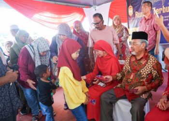 TAJUDDIN Abdul Rahman menyampaikan duit raya kepada kanak-kanak pada majlis rumah terbuka Aidilfitri di kediamannya di Kampung Gajah. - UTUSAN/ZULFACHRI ZULKIFLI