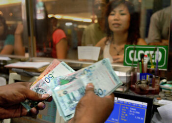 Seorang pengurup wang mengira wang kertas ringgit Malaysia sementara pelanggan menunggu di kiosk pengurup wang di Kuala Lumpur. - AFP