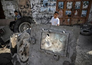 KANAK-kanak Palestin melihat serpihan kenderaan perisai Israel yang musnah dalam serbuan di bandar Jenin di Tebing Barat.-AFP
