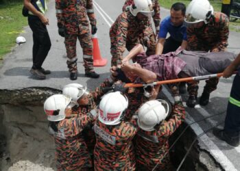 ANGGOTA bomba mengangkat naik penunggang motosikal yang terbabas dalam longkang di jalan yang mendap di Taiping hari ini. - UTUSAN/IHSAN JBPM