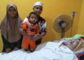 MUHAMMAD Syakir Amin memangku adiknya, Muhammad Zakwan Adha serta Nurul Umairah di samping ibu mereka, Nurul Azhani Abu Hassan @ Hussain yang koma hampir dua tahun ketika ditemui di Kampung Teloi Tua, Sik.