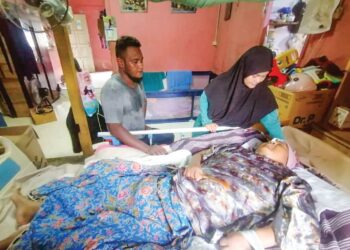 SHAHIYANA Md. Salleh menguruskan ibu mentuanya, Rasidah Tahir yang terlantar akibat serangan angin ahmar di rumah mereka di PPRT Bukit Ara, Hulu Terengganu, kelmarin. – UTUSAN/NOOR HAYATI MAMAT
