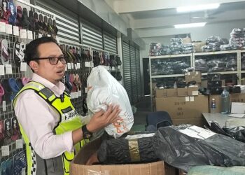 KAMALLUDIN Ismail menunjukkan sebahagian barang yang dirampas dalam serbuan di premis yang dijadikan stor penyimpanan barangan tiruan di Taman Rishah Indah, Ipoh semalam. - UTUSAN