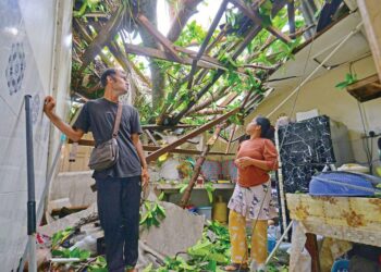 MUHAMMAD Adriy Pariani (kiri) bersama anaknya melihat atap rumah sewa mereka yang rosak akibat dihempap pokok tumbang di Kampung Telok Kemang, Port Dickson, Negeri Sembilan, semalam.
