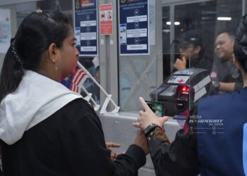 SEORANG pengembara mengimbas kod QR dalam telefon bimbit sambil dibantu oleh pegawai imigresen di Kompleks Sultan Abu Bakar, Iskandar Puteri.