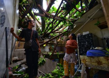 MUHAMMAD Adriy Pariani bersama anaknya melihat pokok yang tumbang dan menghempap bahagian dapur rumahnya dalam kejadian di Kampung Telok Kemang, Port Dickson hari ini.-UTUSAN/MOHD. SHAHJEHAN MAAMIN.
