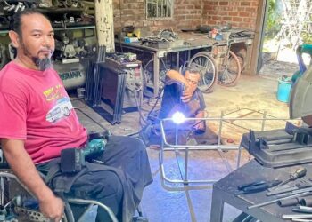 MOHD. Ariff Abdullah di samping pembantunya yang juga OKU menyiapkan tempahan ubah suai motosikal roda tiga di bengkelnya di Alor Mengkudu, Alor Setar. - UTUSAN/JAMLIAH ABDULLAH