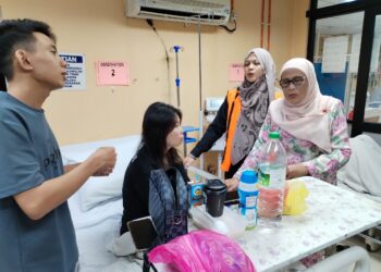 KALSOM Noordin bertanyakan sesuatu kepada Caterina Lee yang mendapat rawatan sambil diperhatikan Kevin Lem Wee di Wad Kecemasan Hospital Melaka. - UTUSAN/AMRAN MULUP