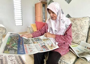 HABIBAH Ismail melihat laporan keratan akhbar Utusan Malaysia yang disimpannya berhubung tragedi MH17 yang mengorbankan anaknya ketika ditemui di Kampung Kelompang, Alor Setar, Kedah. – UTUSAN/ JAMLIAH ABDULLAH