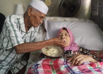 MOHD. Nor Mohd. Laham menyuap makanan kepada isterinya, Norhalime Sanin yang terlantar ketika ditemui di rumahnya di Flat Taman Semarak, Nilai, Seremban.-UTUSAN/NUR SHARIEZA ISMAIL.