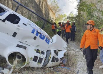 PENYELAMAT memeriksa serpihan sebuah helikopter selepas ia terhempas di Badung, Pulau Bali di Indonesia, semalam.- AGENSI
