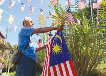 HAMZAH Mohamad menghias pokok bunga Orkid Harimau yang ditanamnya dengan Jalur Gemilang ketika ditemui di Kampung Chenong Ulu, Rembau, semalam.-UTUSAN/NOR AINNA HAMZAH.