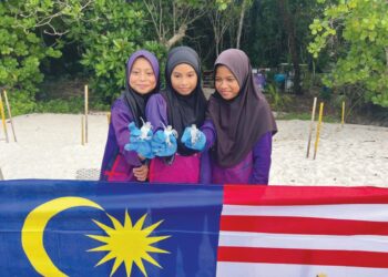 NUR Afrina Batrisya (kiri) menunjukkan anak penyu yang dilepaskan sebagai simbolik hari kebangsaan di Pantai Chagar Hutang, Pulau Redang, kelmarin. – UTUSAN/TENGKU DANISH BAHRI TENGKU YUSOFF