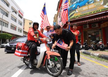 MURTADHATUMIZI Mustapa (kanan) meletakan Jalur Gemilang di sebuah motosikal sebagai kempen menyemarakan lagi sambutan kemerdekaan negara ke-67 di Kota Bharu, Kelantan hari ini.-UTUSAN/KAMARUL BISMI KAMARUZAMAN.