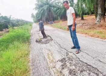 PENDUDUK melihat keadaan jalan yang rosak akibat mendapan 
di Hutan Melintang, Bagan Datuk. – UTUSAN/AIN SAFRE BIDIN