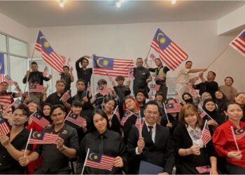MUHAMMAD Nasrullah Yahya (baris hadapan, empat dari kanan) bersama tukang gunting rambut dari kedai gunting rambut dan salun, Team C Cut mengibarkan Jalur Gemilang sempena sambutan Bulan Kebangsaan di Labu, Seremban, semalam.