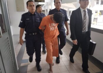 TERTUDUH diiringi anggota polis ketika dibawa keluar dari Mahkamah Majistret Ayer Keroh, Melaka.