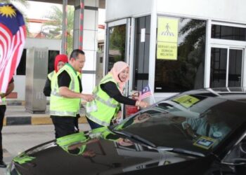 SUAIBAH Harun (kanan) memasang Jalur Gemilang di salah sebuah kenderaan di Plaza Tol Gemuruh, Lebuhraya Pantai Timur 2 (LPT2), Kuala Nerus, semalam. - UTUSAN/KAMALIZA KAMARUDDIN