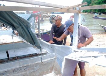 NUR MUHAMMAD AZRI Mustafa (kiri) dan Mohd. Sumeley Majid meninjau keadaan bot mereka yang karam dibadai ombak dan ribut berhampiran perairan Pulau Upeh, Melaka. 
– UTUSAN/AMRAN MULUP