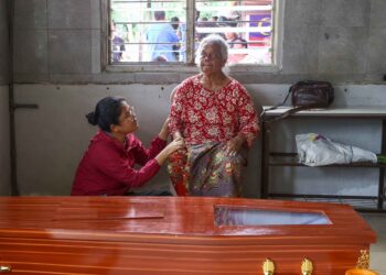 ISTERI mendiang Apot Saad, Krig Sudin di sisi keranda suaminya di rumah mereka di Kampung Batu Berangkai di Kampar hari ini. - UTUSAN/MUHAMAD NAZREEN SYAH MUSTHAFA