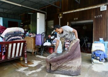 MOHD. Izham Abdul Manaf mencuci dan menjemur barangan di rumahnya yang ditenggelami banjir ketika air mula surut di Kampung Suka Menanti, Alor Setar semalam. -UTUSAN/ SHAHIR NOORDIN